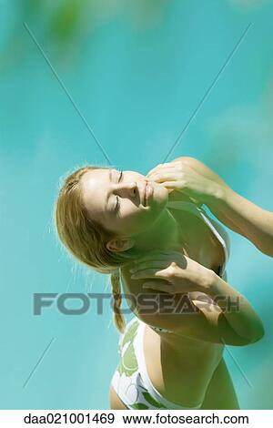 Stock Photo - Young woman standing in bikini with hands on shoulders, eyes closed, high angle view, blur in foreground. Fotosearch