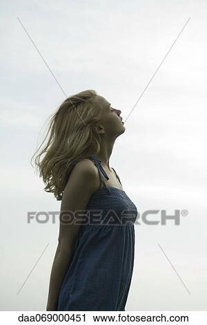 Stock Image - Young woman standing in breeze with eyes closed. Fotosearch