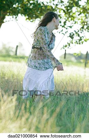 Picture - Young woman standing in field, looking over shoulder. Fotosearch