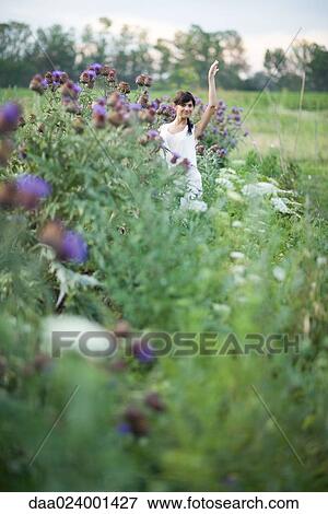 Stock Photo - Young woman standing in flower garden, waving, in mid distance. Fotosearch