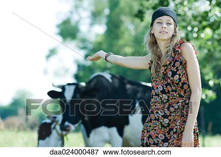 Young woman standing in front of cows, arm outstretched behind her, smiling at camera View Large Photo Image Stock Photo - Young woman standing in front of cows, arm outstretched behind her, smiling at camera. Fotosearch