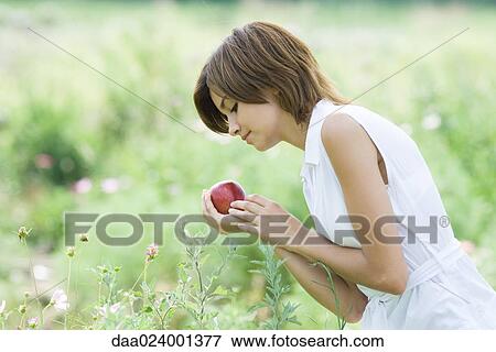 Stock Photo - Young woman standing in garden, holding apple. Fotosearch
