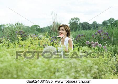 Stock Photography - Young woman standing in garden, holding slice of watermelon. Fotosearch