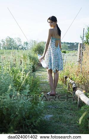 Young woman standing in garden with bottle of water, looking over shoulder at camera View Large Photo Image Stock Image - Young woman standing in garden with bottle of water, looking over shoulder at camera. Fotosearch