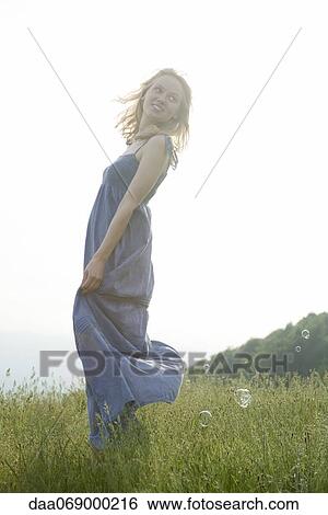 Young woman standing in meadow on breezy day, bubbles floating around her View Large Photo Image Stock Photograph - Young woman standing in meadow on breezy day, bubbles floating around her. Fotosearch