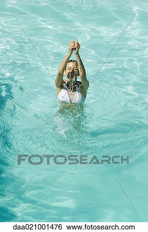 Stock Photograph - Young woman standing in pool, arms over head and eyes closed, full length, high angle view. Fotosearch