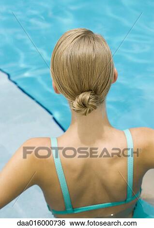 Stock Photograph - Young woman standing in pool, rear view, head and shoulders. Fotosearch