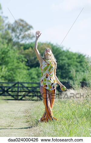 Young woman standing in rural field with arm raised, looking up, apple in hand View Large Photo Image Stock Photograph - Young woman standing in rural field with arm raised, looking up, apple in hand. Fotosearch