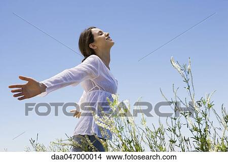 Young woman standing in tall grass with arms out, eyes closed View Large Photo Image Picture - Young woman standing in tall grass with arms out, eyes closed. Fotosearch