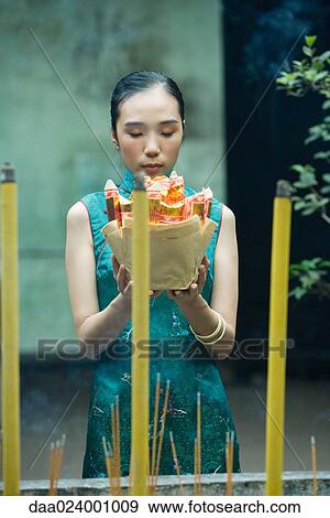 Young woman standing in temple courtyard, holding up religious offering, eyes closed View Large Photo Image Stock Photo - Young woman standing in temple courtyard, holding up religious offering, eyes closed. Fotosearch