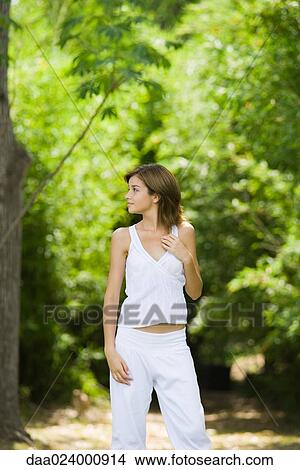 Young woman standing in woods, looking over shoulder and smiling View Large Photo Image Picture - Young woman standing in woods, looking over shoulder and smiling. Fotosearch
