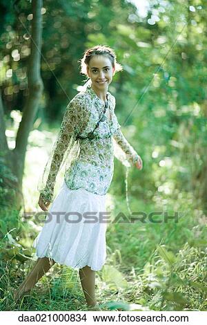 Picture - Young woman standing in woods, smiling at camera. Fotosearch