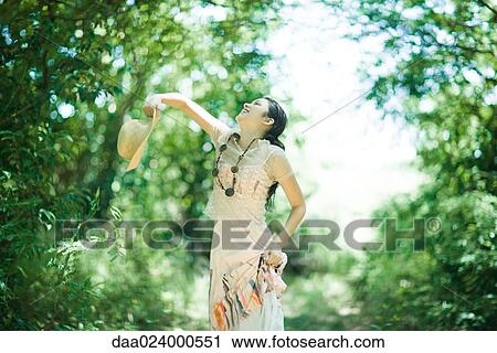 Young woman standing in woods, throwing up sunhat View Large Photo Image Stock Image - Young woman standing in woods, throwing up sunhat. Fotosearch