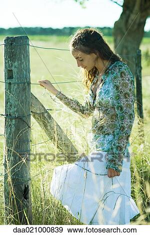 Young woman standing next to rural fence, looking down View Large Photo Image Stock Photo - Young woman standing next to rural fence, looking down. Fotosearch