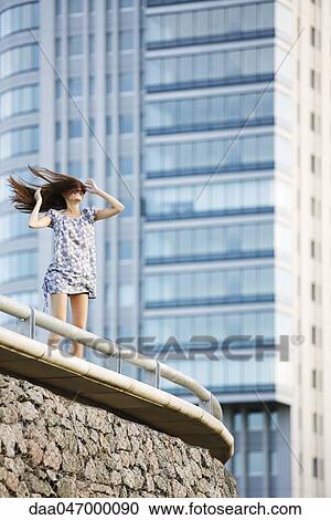 Young woman standing on balcony, wind blowing long hair across face View Large Photo Image Stock Image - Young woman standing on balcony, wind blowing long hair across face. Fotosearch