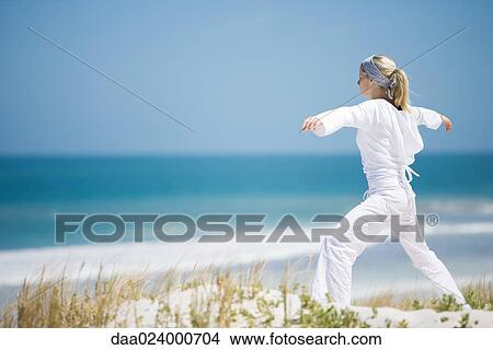 Young woman standing on dunes, exercising, ocean in background View Large Photo Image Picture - Young woman standing on dunes, exercising, ocean in background. Fotosearch