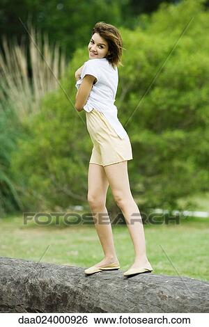 Young woman standing on log, smiling over shoulder at camera View Large Photo Image Stock Photograph - Young woman standing on log, smiling over shoulder at camera. Fotosearch
