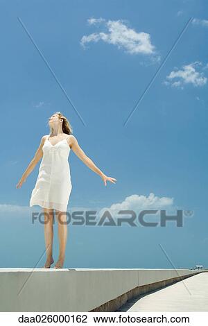 Young woman standing on tiptoe on low wall, arms out, head back View Large Photo Image Stock Image - Young woman standing on tiptoe on low wall, arms out, head back. Fotosearch