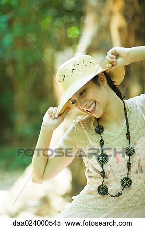 Young woman standing outdoors, putting on sunhat, smiling View Large Photo Image Stock Photography - Young woman standing outdoors, putting on sunhat, smiling. Fotosearch