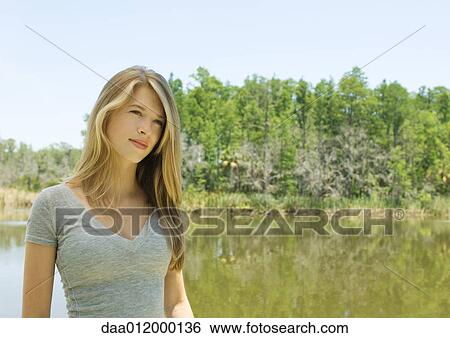 Stock Photograph - Young woman standing outdoors, waist up. Fotosearch