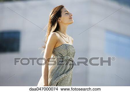 Picture - Young woman standing outdoors with head back, eyes closed. Fotosearch