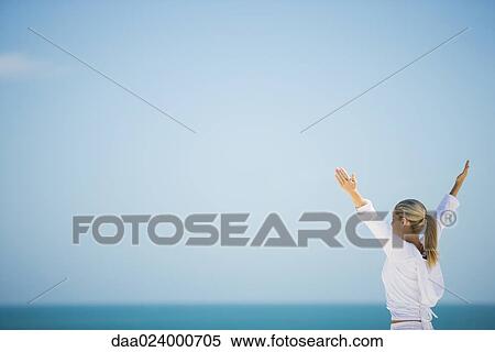 Young woman standing with arms out, ocean horizon in background View Large Photo Image Stock Photography - Young woman standing with arms out, ocean horizon in background. Fotosearch