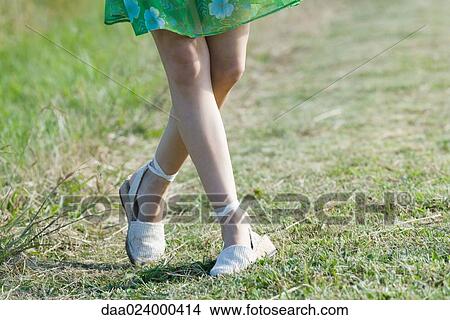 Picture - Young woman standing with legs crossed at knees, cropped view. Fotosearch