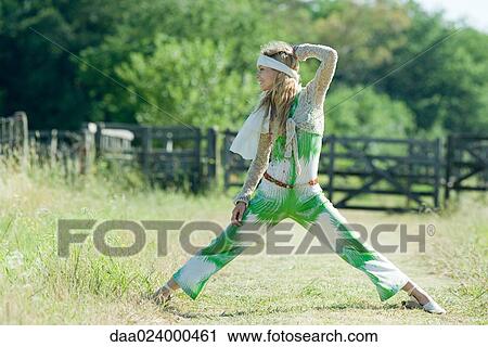 Stock Image - Young woman standing with legs wide apart, in rural field, looking away. Fotosearch