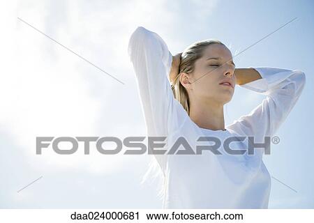 Young woman standing with sky in background, pushing hair back, eyes closed, low angle view View Large Photo Image Stock Image - Young woman standing with sky in background, pushing hair back, eyes closed, low angle view. Fotosearch