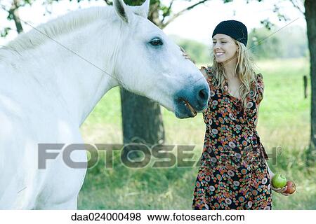 Young woman touching horse, holding apples View Large Photo Image Stock Photo - Young woman touching horse, holding apples. Fotosearch