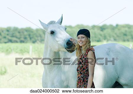 Young woman touching horse, smiling at camera View Large Photo Image Stock Image - Young woman touching horse, smiling at camera. Fotosearch