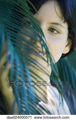 Stock Image - Young woman touching palm leaf, cropped portrait. Fotosearch