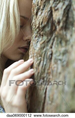 Stock Image - Young woman touching tree with eyes closed. Fotosearch