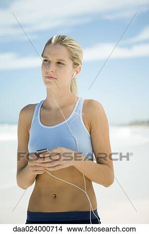 Young woman using MP3 player on beach, wearing active wear View Large Photo Image Picture - Young woman using MP3 player on beach, wearing active wear. Fotosearch
