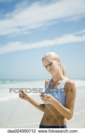 Stock Image - Young woman using MP3 player on beach, wearing active wear. Fotosearch