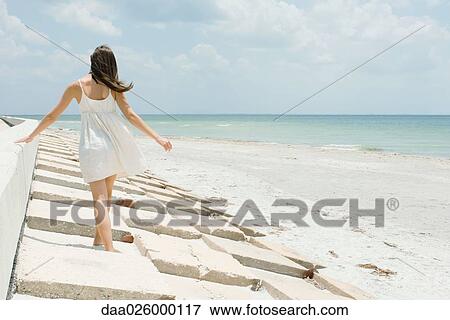 Young woman walking along low wall at the beach, rear view View Large Photo Image Stock Photo - Young woman walking along low wall at the beach, rear view. Fotosearch