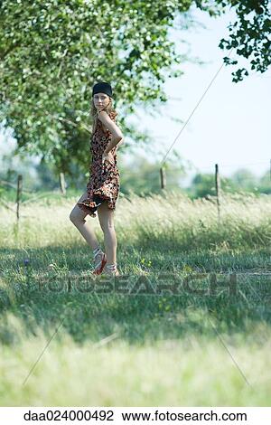 Stock Image - Young woman walking along rural path, looking over shoulder. Fotosearch