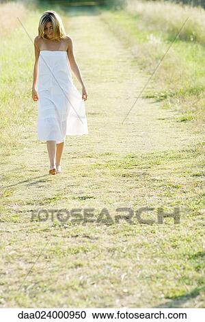 Stock Image - Young woman walking barefoot along rural path. Fotosearch
