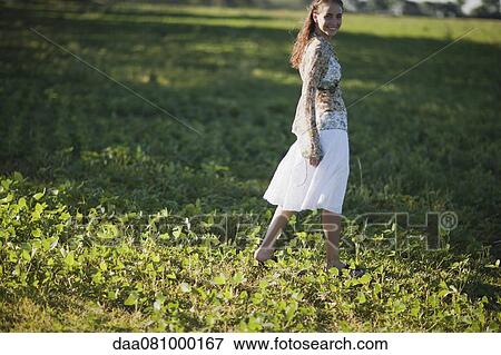 Young woman walking in field, looking over shoulder at camera View Large Photo Image Stock Photo - Young woman walking in field, looking over shoulder at camera. Fotosearch