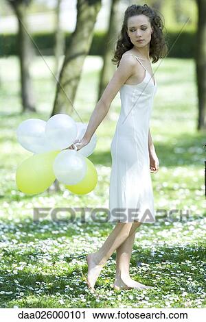 Young woman walking in field of flowers, holding balloons behind back, looking over shoulder View Large Photo Image Stock Image - Young woman walking in field of flowers, holding balloons behind back, looking over shoulder. Fotosearch