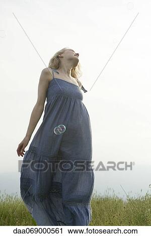 Stock Image - Young woman walking in meadow, bubbles floating around her. Fotosearch