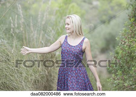 Young woman walking in nature, touching tall grass View Large Photo Image Stock Photograph - Young woman walking in nature, touching tall grass. Fotosearch