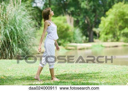 Stock Image - Young woman walking in park, looking up. Fotosearch