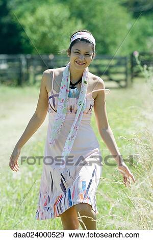 Stock Photo - Young woman walking in rural setting, smiling at camera. Fotosearch