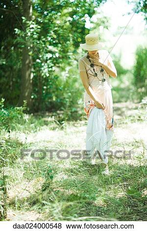 Stock Photo - Young woman walking in woods, lifting skirt, looking down. Fotosearch