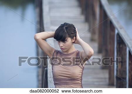 Stock Image - Young woman walking on dock with hands in hair. Fotosearch