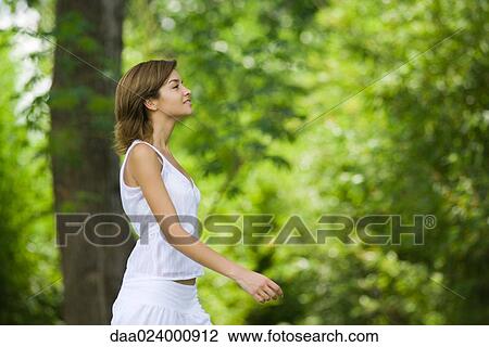 Stock Image - Young woman walking outdoors, side view. Fotosearch