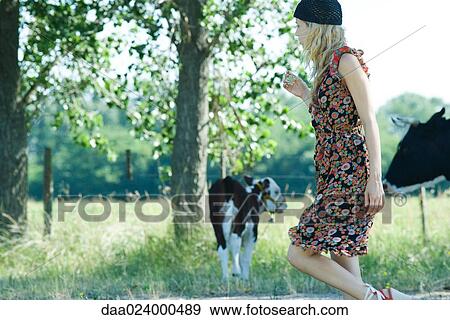 Stock Photo - Young woman walking past cows, side view. Fotosearch