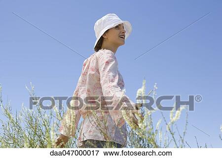 Stock Photo - Young woman walking through field of tall grass with arms out, smiling. Fotosearch