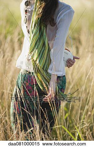 Stock Photography - Young woman walking through field with portable CD player, rear view. Fotosearch